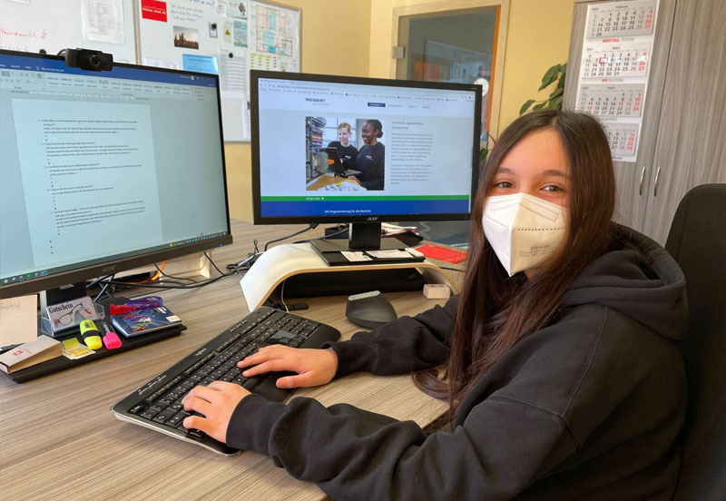 Eine Schülerin mit Mundschutz sitzt vor einem PC Monitor